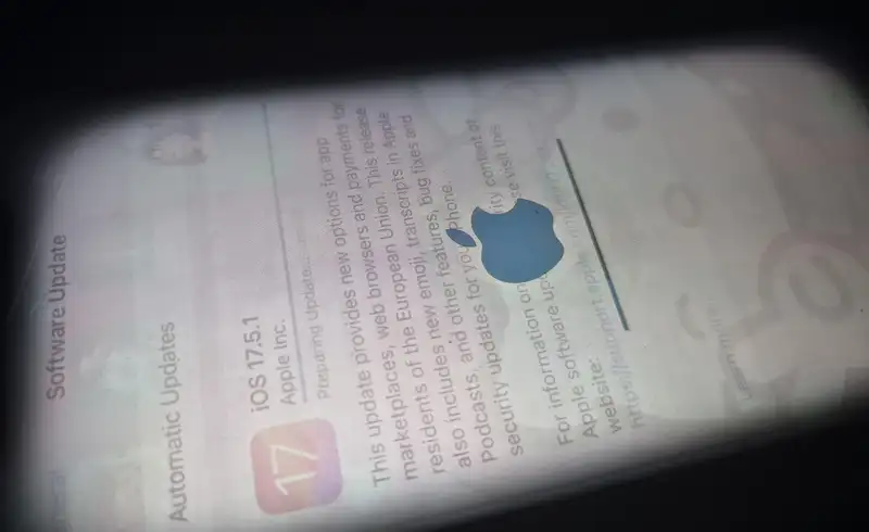 Macro extrem pe un display iPhone OLED care arata image retention sever: logo-ul Apple si elemente din meniul Software Update raman vag vizibile ca fantome pe ecran cu un alt continut