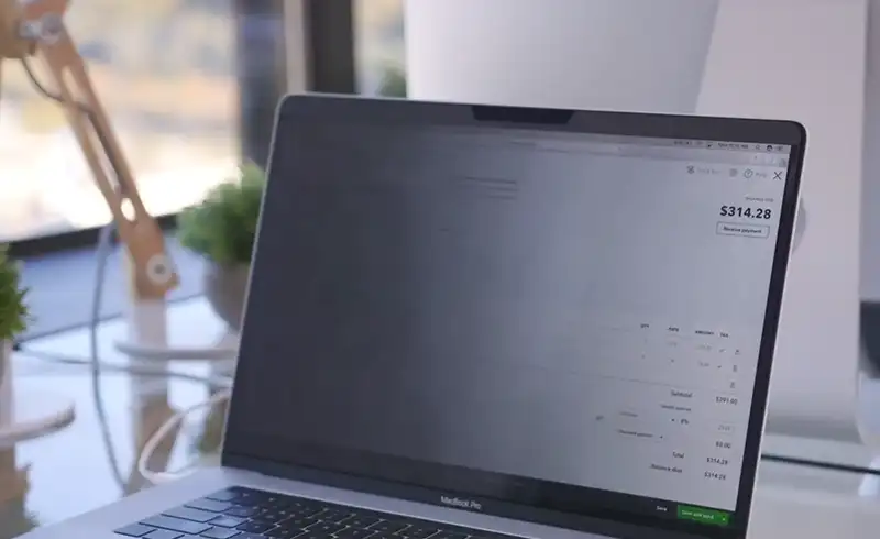 MacBook Pro fotografiat dintr-un unghi oblic — ecranul afiseaza o aplicatie de facturare cu textul aproape ilegibil, culorile spalacite si contrastul pierdut din cauza unghiului de vizualizare slab al panoului TN sau IPS de calitate inferioara