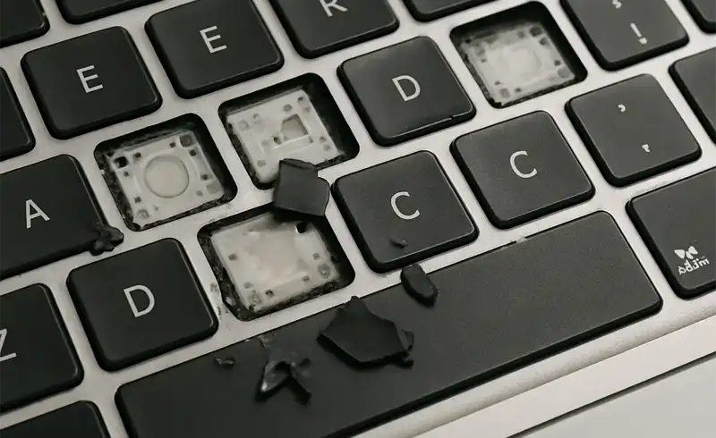 Macro pe o tastatură MacBook cu taste scoase și chunks de plastic rupte — exemplu de tastatură distrusă