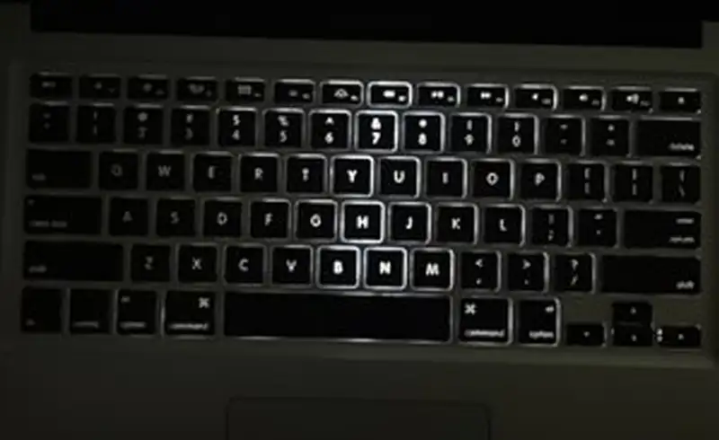 Tastatura MacBook fotografiata in intuneric — retroiluminarea LED functioneaza doar pe randul central de taste (Y, G, H, B, N, M), restul tastelor raman complet intunecate, semn de panou LED defect sau driver controller necalibrat